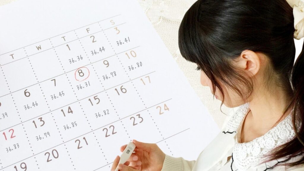 基礎体温計を見つめて
いる女性。背景はカレンダー。