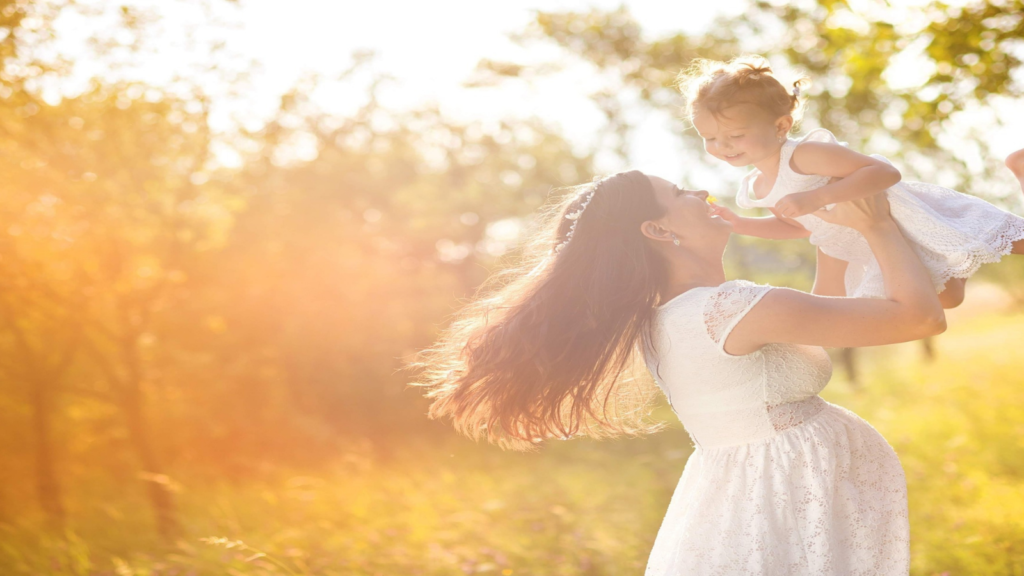木漏れ日の中、女性が女の子を高い高いをしている。