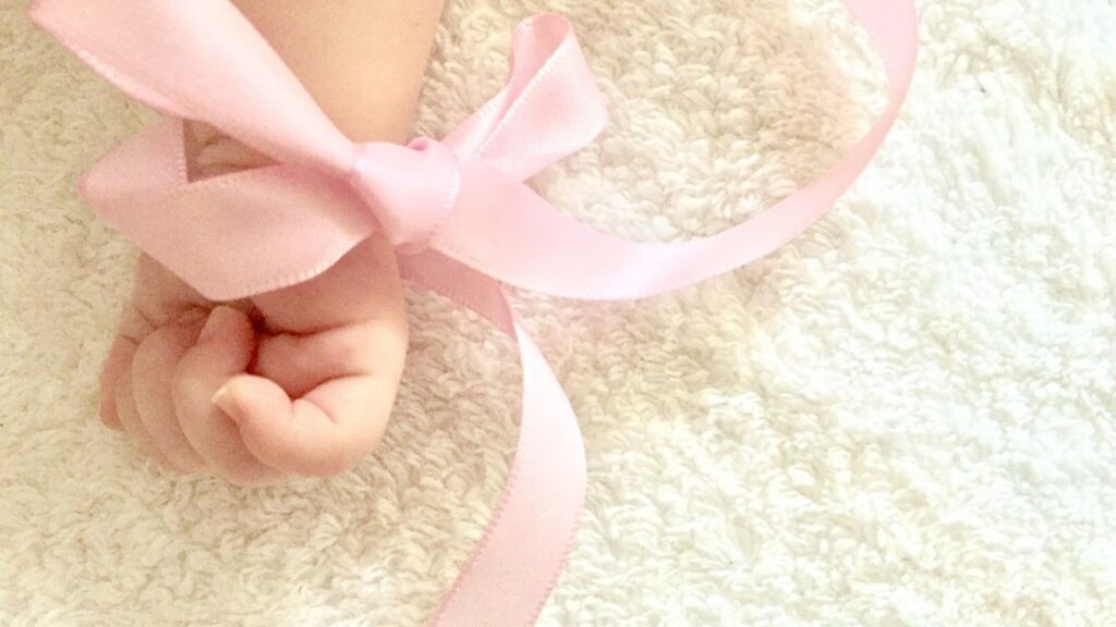 赤ちゃんの手にピンクのリボンを結んでいる。