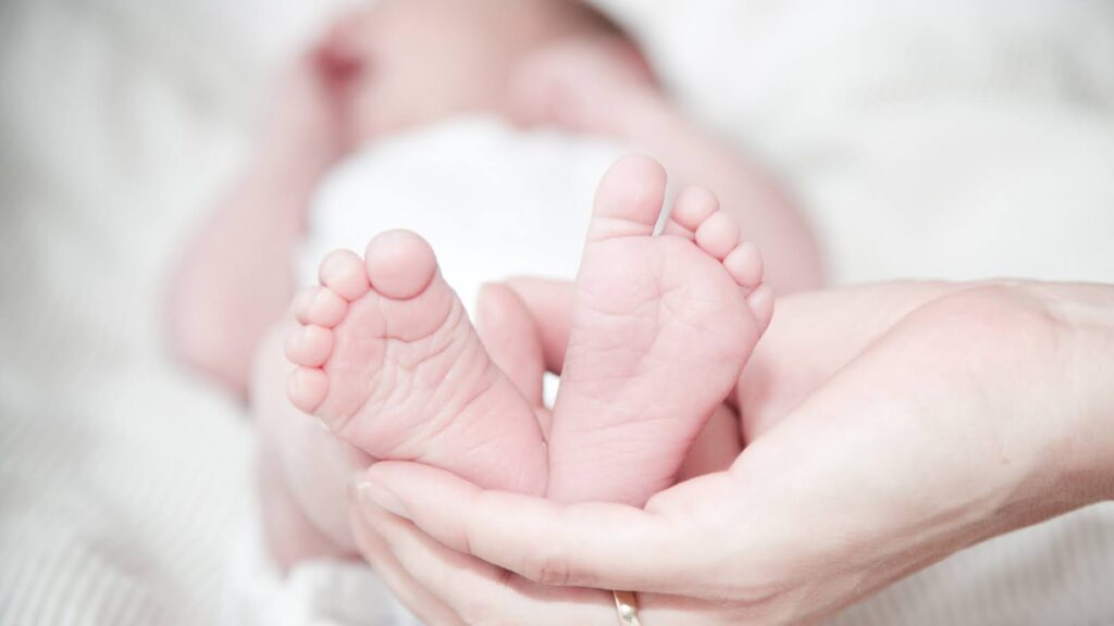 寝ている赤ちゃんのあしを持ち上げている女性の手
