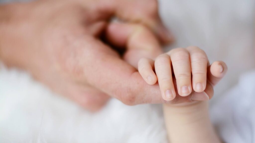 赤ちゃんの小さな手に人差し指を差し込んでいる大人の手