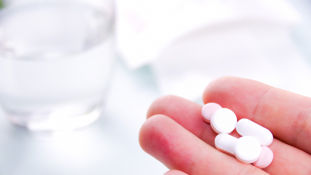 手に錠剤を乗せている。奥にはコップに入った水。